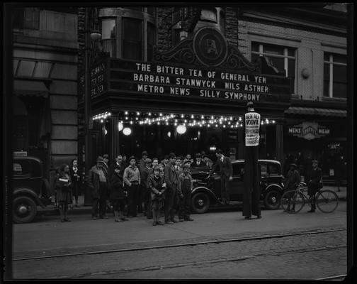Ben Ali Theatre (movie theater), 121 East Main, exterior, street scene; man on stilts as part of a theater promotion, a sign on his back reads: 