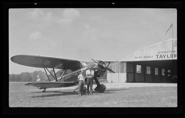 Cool Meadows; Lexington Airport; two men standing beside airplane that is parked outside of hanger; Taylor Cub Sales