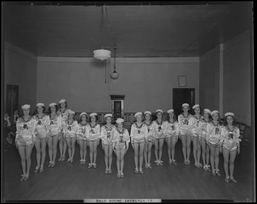 Juanita Crutcher; Dance Group at Mac. Hall, girls dressed in outfits with hats on lined up in a row, interior of empty room