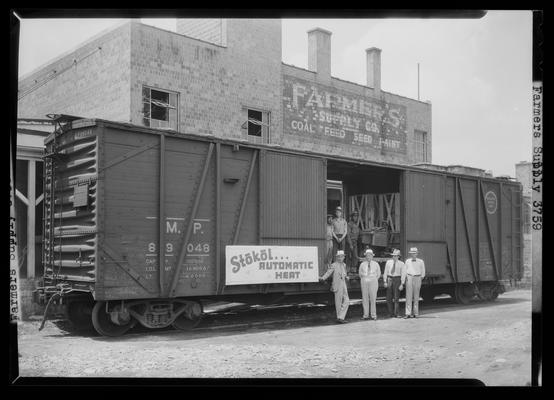 Farmer's Supply Company; men standing at the exterior of boxcar and brick building