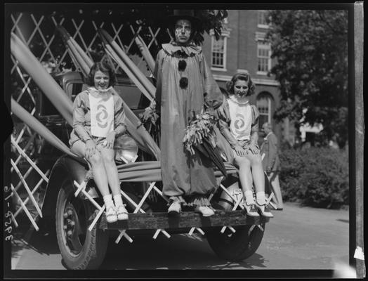 May Queen Activities (1939 Kentuckian) (University of Kentucky), two (2) girls in costume sitting on the front of a truck with a clown