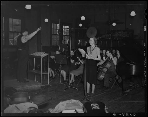 Miscellaneous (1939 Kentuckian) (University of Kentucky); conductor standing before the orchestra (band members), woman standing in front of a microphone
