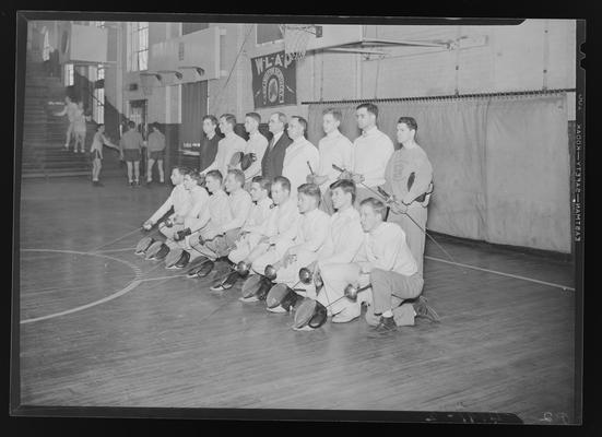 Fencing Team (1939 Kentuckian) (University of Kentucky); team group portrait on the basketball court of the gymnasium, group of men playing basketball in the background