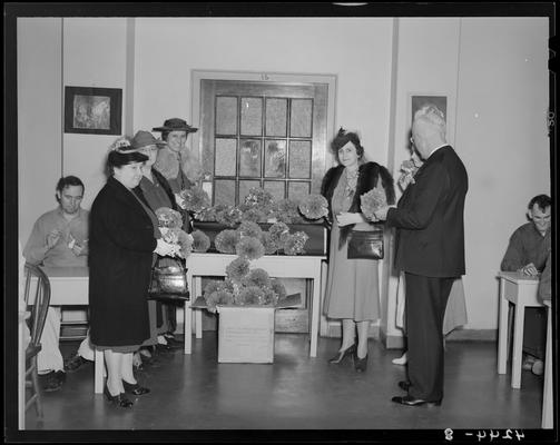 Veterans Hospital; interior, table with flower bouquets; group of women and a man are holding and looking over the bouquets