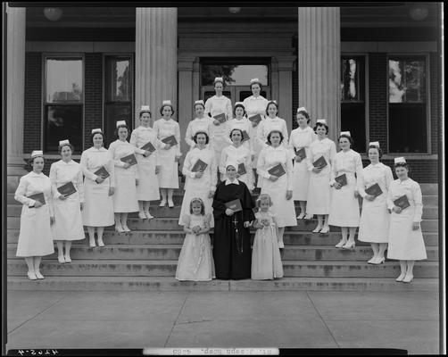 Saint Joseph Hospital, 544 West Second (2nd) Street; nurses' graduation, nurse group portrait, nurses standing on steps of building, holding diplomas, two young girls and a nun standing in front of group