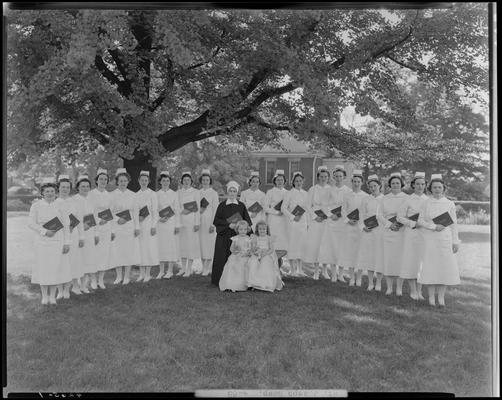 Saint Joseph Hospital, 544 West Second (2nd) Street; nurses' graduation, nurse group portrait, nurses standing outside underneath a tree, holding diplomas, two young girls and a nun standing in front of group