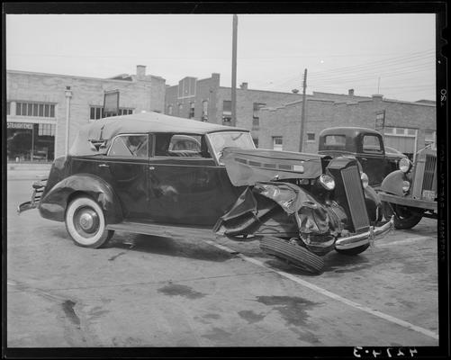 John Crosby; damaged (wrecked) car parked in lot, damaged passenger side and front of vehicle, front view