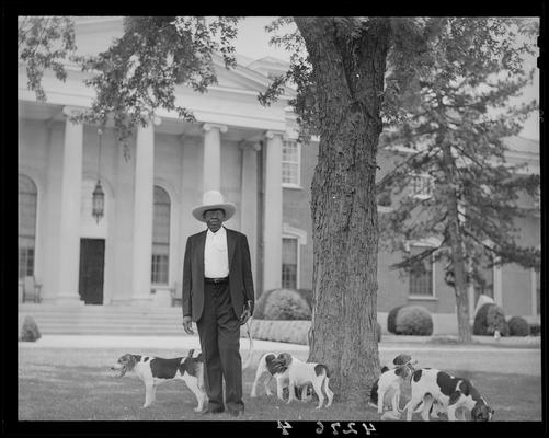 Spindletop Farm; man standing besides a tree in front of a large mansion (house), group of dogs gathered next to man