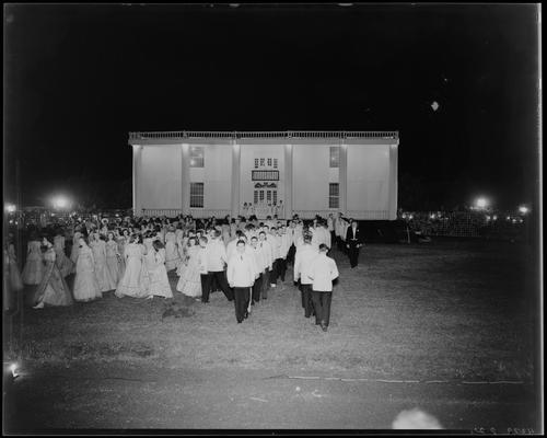 Centre College (Danville); Festival; large group of men and women in formal dress (attire) parading on the grass (lawn) in front of a large building; night scene