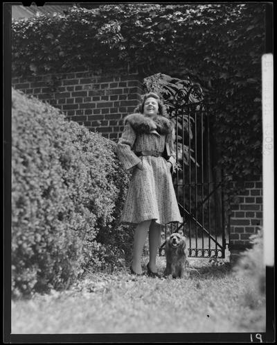 B.B. Smith & Company, 264 West Main; woman in a fur coat standing next to an iron gate (modeling), dog standing at her feet