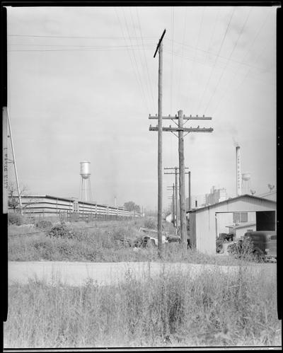 John Crosby; telephone poles, view of a row of telephone poles; water tower and a large building can be seen to the left of the telephone poles