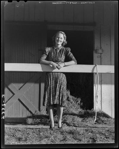 Wildcat Book; girl standing next to a barn, leaning on a wooden railing (modeling)
