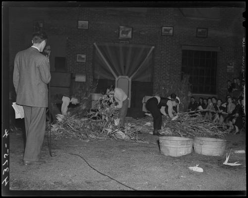 Queen of Stock Festival, (1940 Kentuckian) (University of Kentucky); festival activities, two men are shucking corn while an announcer speaks into a microphone