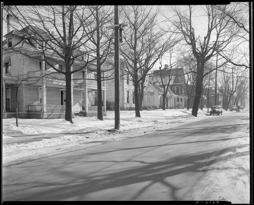 John S. Yellman; post accident scene photograph, view of tree-lined street and houses; cars parked next to curb; man pushing a cart down the street