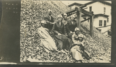 7 men and women at a coal camp sitting on the side of a large mound