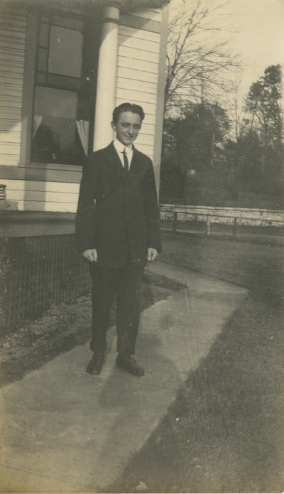 young man wearing a suit and standing on the walkway to a house