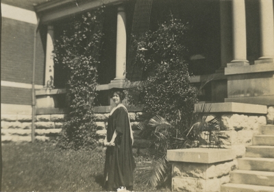 a woman standing in front of a building wearing graduation cap and gown (appears to be the same woman as in image #25 and #26)