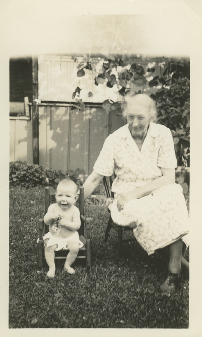 an older woman and a baby sitting in chairs in the yard