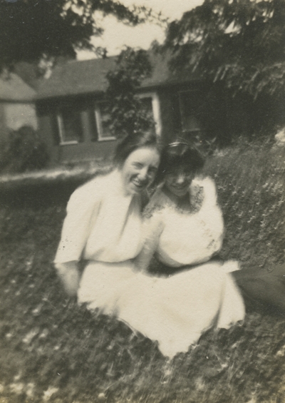 2 women sitting in the yard outside a house