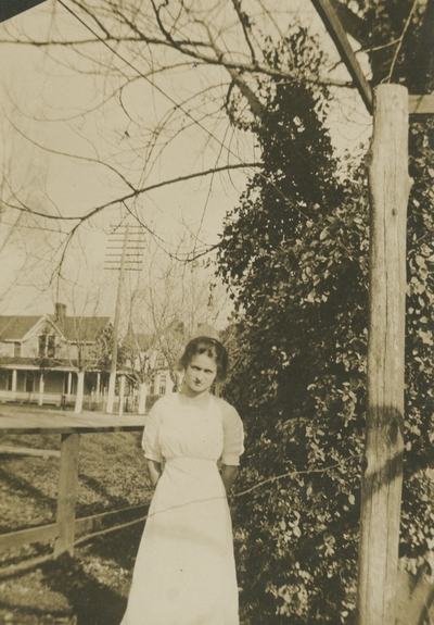 a woman standing by fence with a house in the background