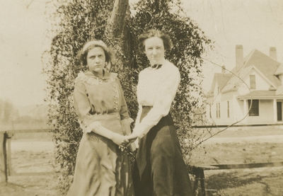 2 women (appear to be the same women as in image #59) standing next to a tree