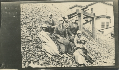 7 men and women at a coal camp sitting on the side of a large mound