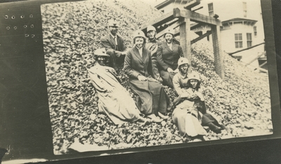 7 men and women at a coal camp (appears to be the same people as item #6) sitting on the side of a large mound
