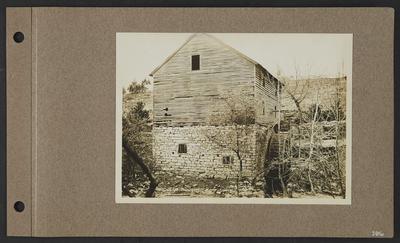 Wood and stone building with mill, barred windows, wooden fence in distance