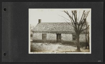 Stone building with shingled room, number                          118 on door, can on ground in front of door, two story building in back left, notation                          Old Crow Station near Danville, Ky
