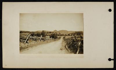 Dirt road with split-rail fencing on left and regular wooden fencing on right