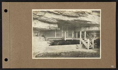 Steps leading to room in cave, lattice covering entrance, sign reads                          No lunching on the grounds, bag draped over low concrete wall