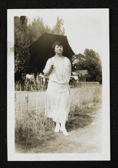 Cora Wilson Stewart standing outside, wearing a white dress and holding a black umbrella