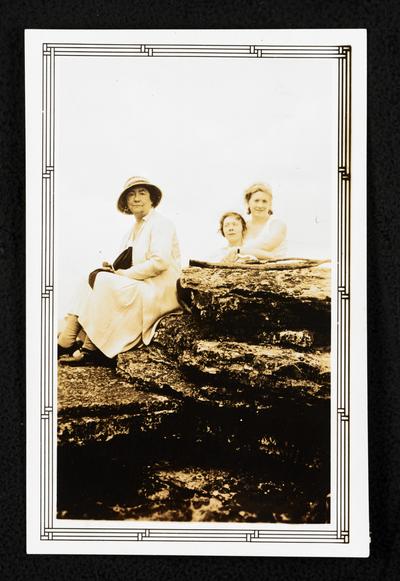 Cora Wilson Stewart and two unidentified woman sitting on large ocean rocks