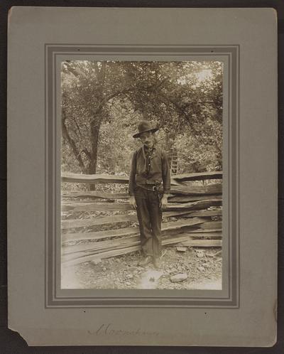 Unidentified male standing in front of a wooden fence. Below the photograph reads: Moonshiner