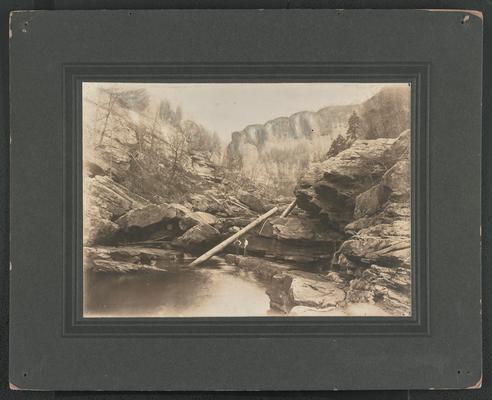 Two unidentified males standing at the bottom of a mountain at a creek. The back of the photograph reads: A scene in the Kentucky mountains