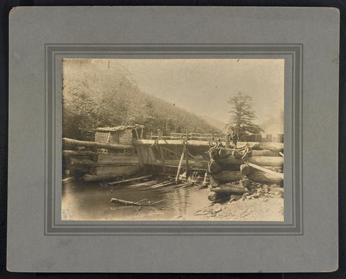 A dam across a small creek, three unidentified males at the top of the dam. The back of the photograph reads: Water Mill