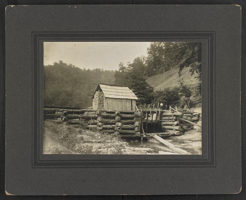 A wooden dam over a creek with two unidentified figures on top. Bottom of the photograph reads: Great Mill- Shelby County, Pike County