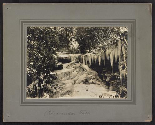 Icicles and snow on mountain rocks and surrounding trees. Bottom of the photograph reads: Rhododendrum Falls