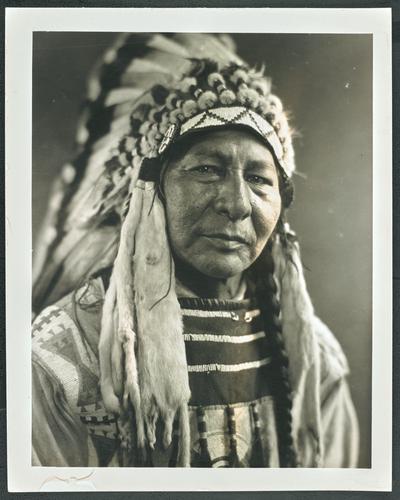 Formal portrait of a man in traditional Native American dress. Back of the photograph identifies him as: Chief Eagle Child