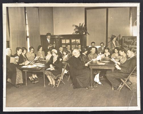 Unidentified adult students, sitting in a classroom reading books