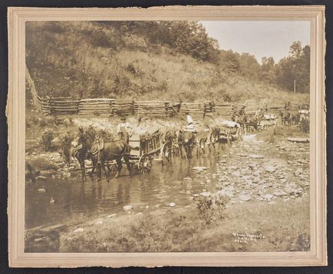 Unidenfitied men steering horse drawn wagons through a creek. Back of the photograph reads: The Mountain Child- His environment. Road in the creek. May do for hauling, but pretty rough for a lad to wade through to school