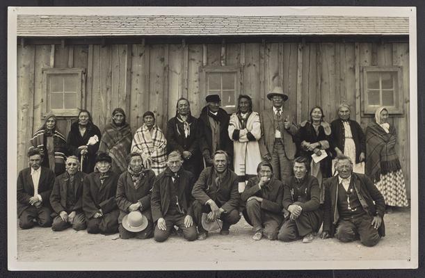 A group of older Native Americans posing outdoors. A typed label on the back reads: Students seventy years of age and older enrolled in illiteracy clinic Blackfeet Indian Reservation