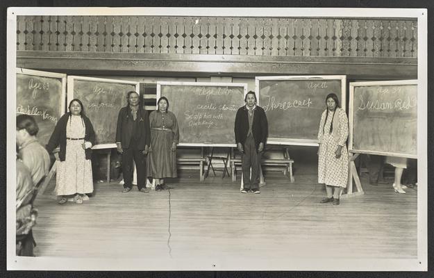 3 women and 2 men standing in front of chalkboards with their names written out. A typed label reads: Contestnats for the prize in writing which was won by 'Scalp Him with His Own Knife'