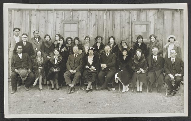 A large group of adults, a typed label on the back of the photograph reads: Teachers -Center Mrs. Cora Wilson Stewart- to the right Mr. C.F. Campbell -to the left Mr. Forrest Stone. Illiteracy Clinic Blackfeet Indian Reservation