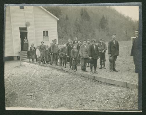 Two lines of children standing in front of a school house, back of the photograph reads: Walk built by children, similar image as item 353