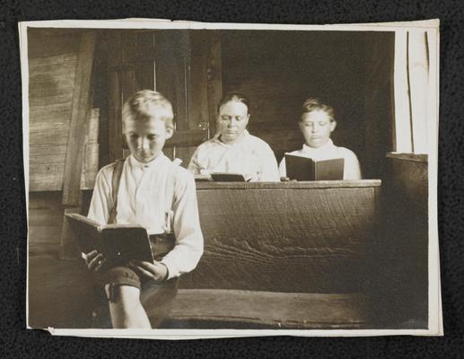 Young boys sitting on benches, reading books in a school house