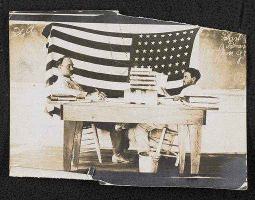 Two men sitting at a table in front of a chalk board, similar photograph to item 365