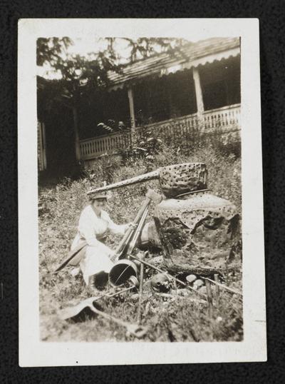 A unidentified woman posing with an ax next to a moonshine still. The back of the photograph reads: This is a real copper still. Has been cut up by the marshals