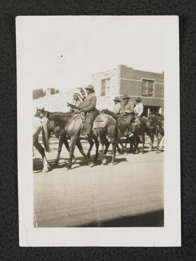 Unidentified group of men riding horses through a street