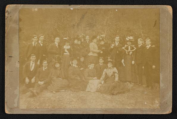 A large group of young adults standing outside, Cora Wilson Stewart is standing third from the right. The back of the photograph lists all others present in the photograph